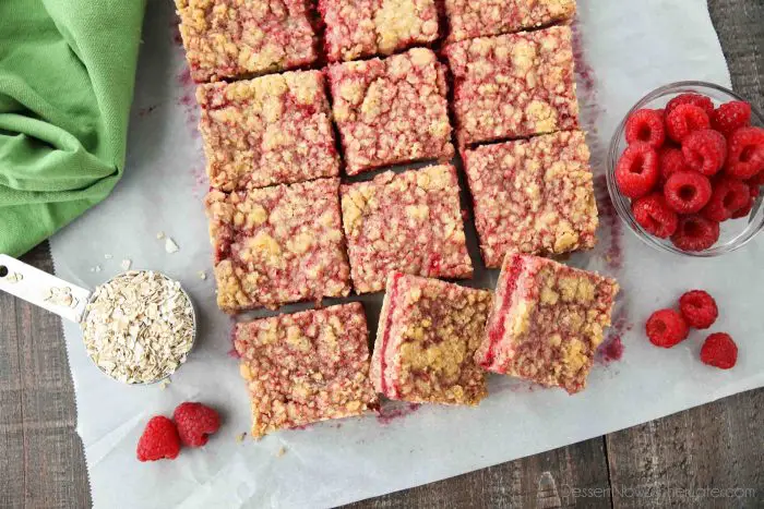Raspberry Crumble Bars on parchment paper with fresh raspberries and oats.