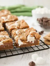 Gooey s'mores bars on a cooling rack with marshmallow fluff and chocolate chips in the center. | Dessert Now Dinner Later