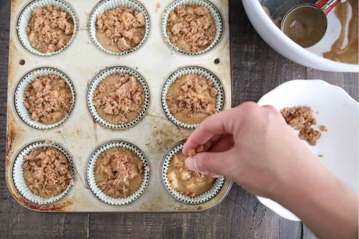 Sprinkling the crumb topping on the apple cinnamon batter filled muffin cups.