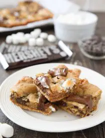 S'mores Cookie Bars are layered with graham crackers, cookie dough with marshmallows, and topped with chocolate bar pieces. It's an ooey gooey melty chocolate s'mores treat!