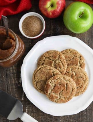 Crinkle topped apple butter cookies on plate with apple butter, cinnamon sugar, and fresh apples nearby.