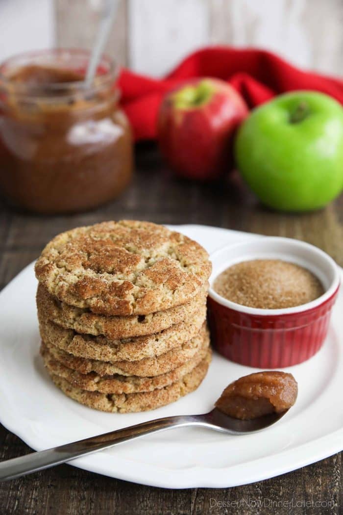 Cookies stacked on top of each other next to a spoonful of apple butter and bowl of cinnamon sugar.