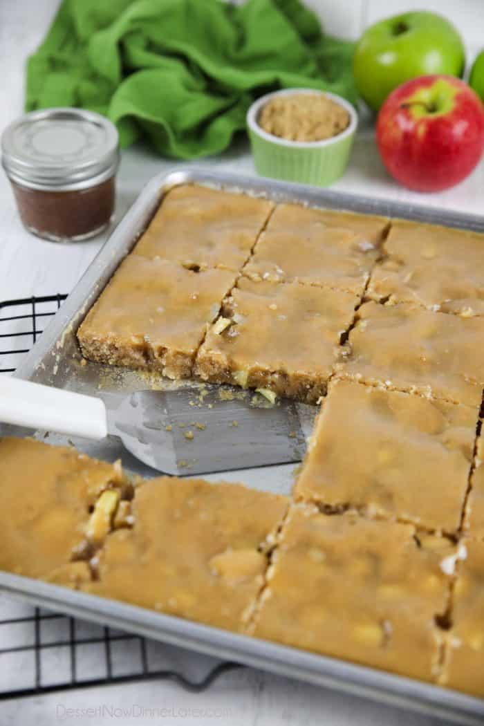 Apple sheet cake with brown sugar glaze in pan with a couple pieces missing.