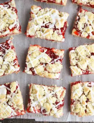 Squares of glazed cherry pie bars on parchment paper and a cooling rack.