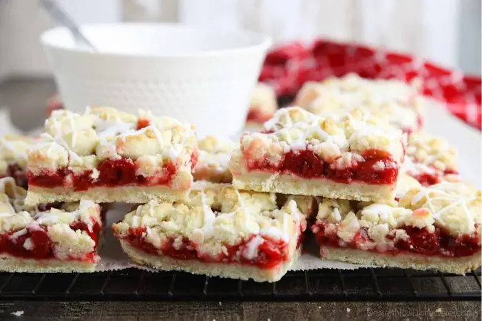 Cherry Pie Bars stacked on top of each other with a bowl of glaze in the background.