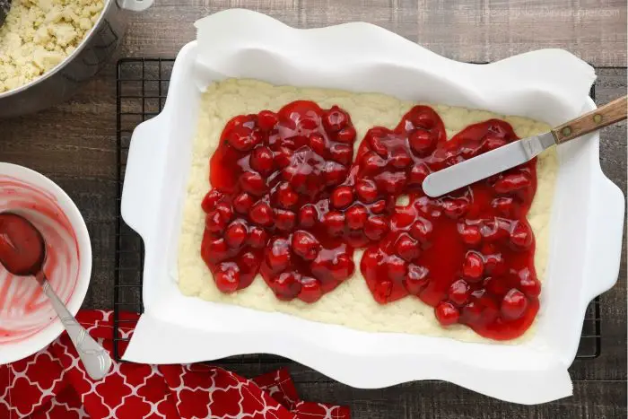 Cherry Pie Filling being spread on shortbread crust with an offset spatula.