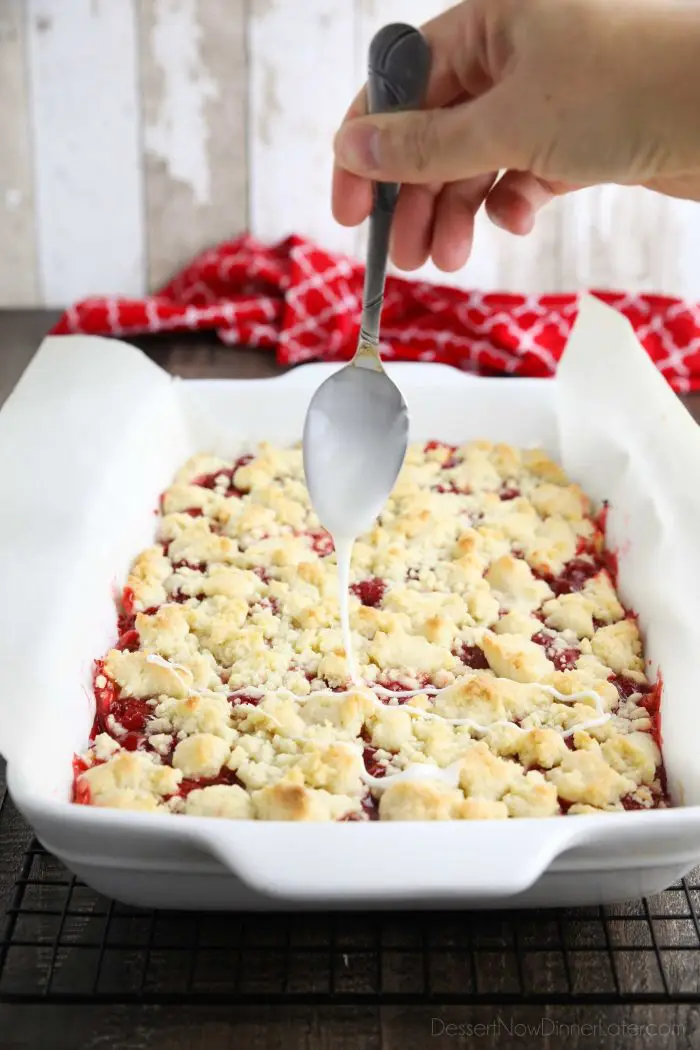 Glaze being drizzled over the top of cherry crumb bars with a spoon.