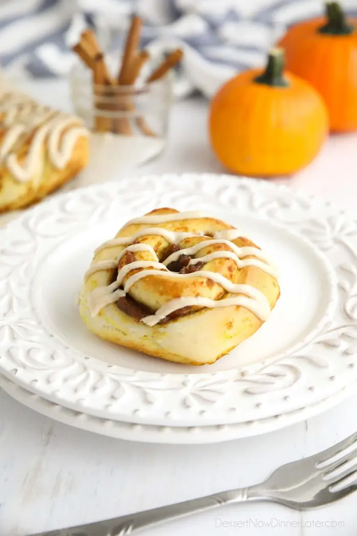 A Pumpkin Pie Cinnamon Roll on a plate with decorative pumpkins and cinnamon sticks in the background.