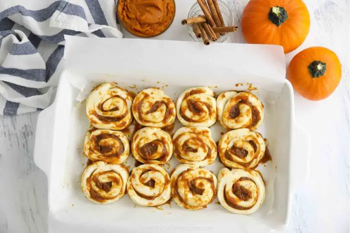 Pumpkin pie cinnamon rolls placed in baking pan fitted with parchment paper ready to bake.