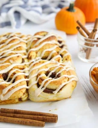 Pumpkin Pie Cinnamon Rolls drizzled with cream cheese frosting sitting on parchment paper.