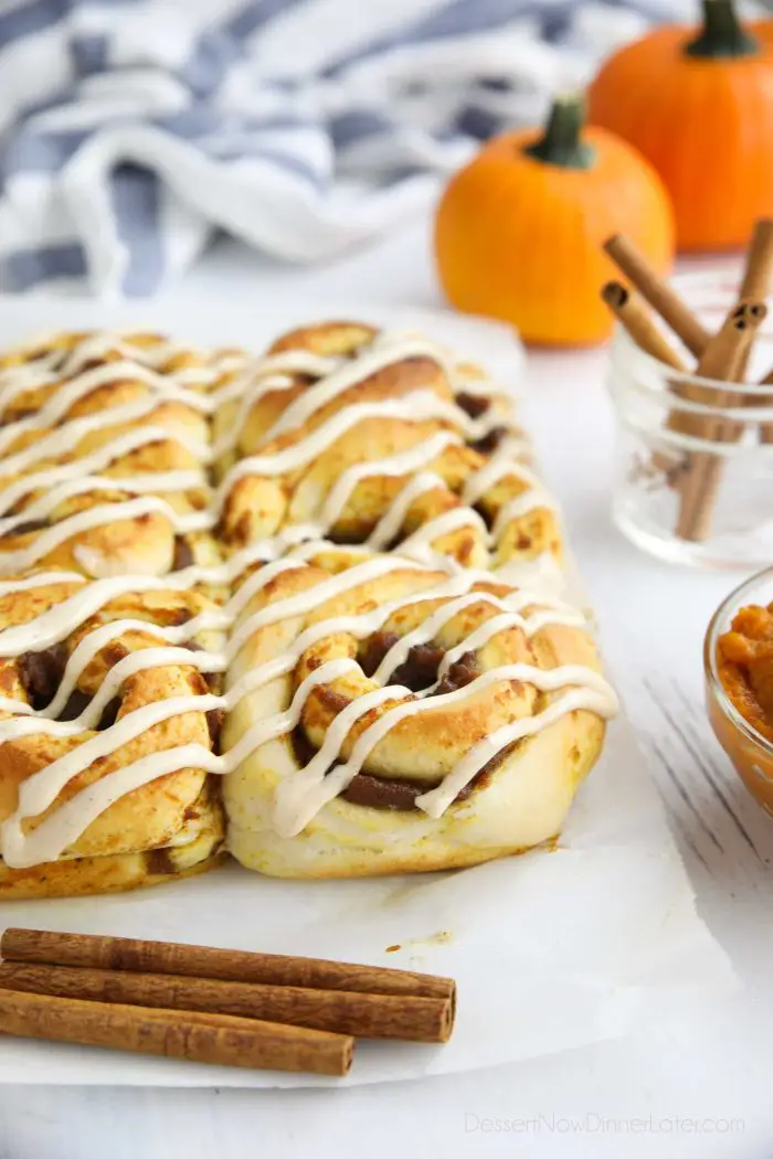 Pumpkin Pie Cinnamon Rolls drizzled with cream cheese frosting sitting on parchment paper.