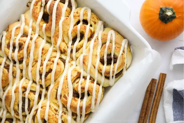 Baked pumpkin cinnamon rolls with cream cheese frosting drizzled on top.