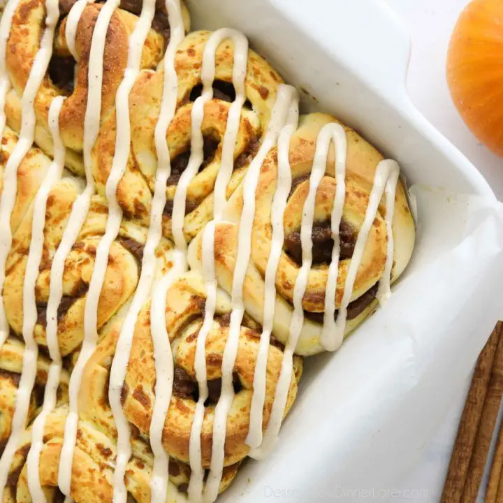 Baked pumpkin cinnamon rolls with cream cheese frosting drizzled on top.