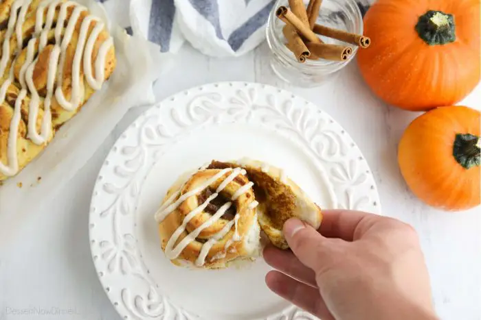 A hand peeling apart the outer layer of the pumpkin cinnamon roll.