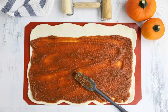 Pumpkin filling being spread on top of rolled out dough.