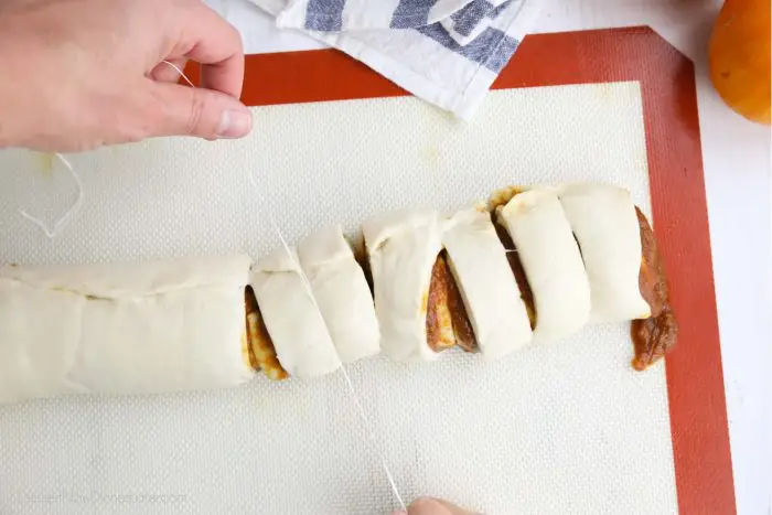 Pumpkin pie cinnamon rolls being cut with floss.