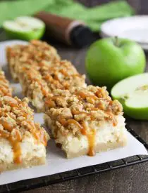 Caramel Apple Cheesecake Bars on a parchment lined wire cooling rack with caramel dripping down the sides.