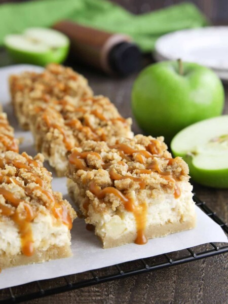 Caramel Apple Cheesecake Bars on a parchment lined wire cooling rack with caramel dripping down the sides.