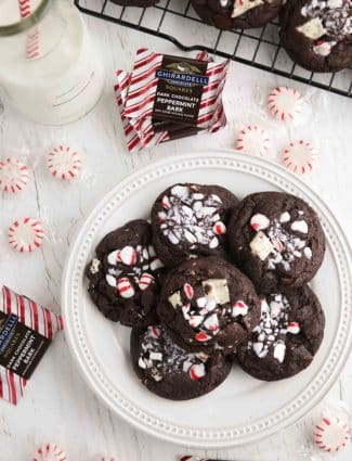 Plate of chocolate peppermint cookies surrounded by round peppermint candies and square peppermint bark chocolates.