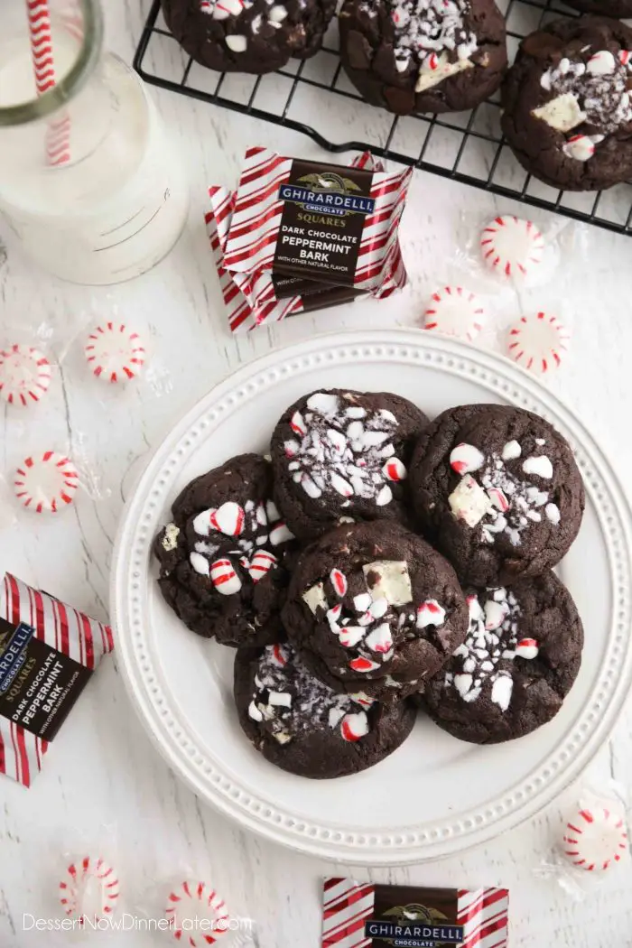 Plate of chocolate peppermint cookies surrounded by round peppermint candies and square peppermint bark chocolates.