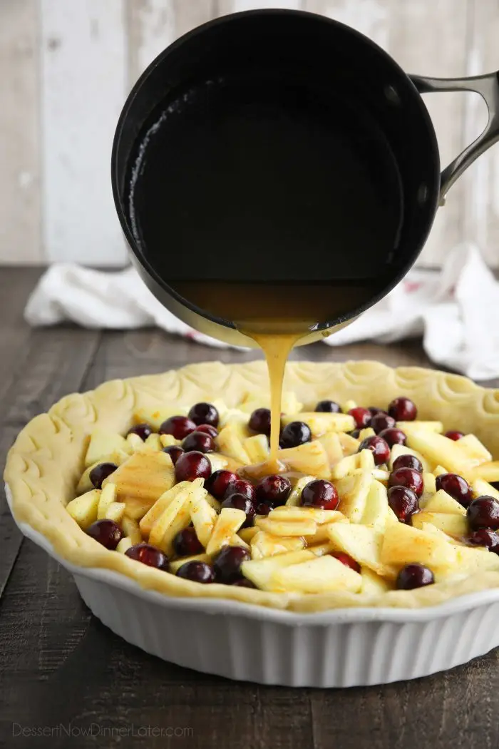 Syrup being poured over cranberries and sliced apples in an unbaked pie crust.