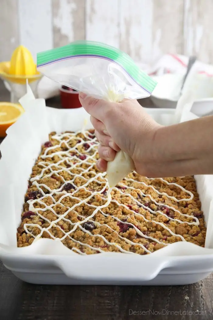 Squeezing orange glaze over baked cranberry bars.