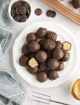 Easy Peanut Butter Balls stacked on a plate. Some drizzled, some plain, and two halves showing the peanut butter interior.