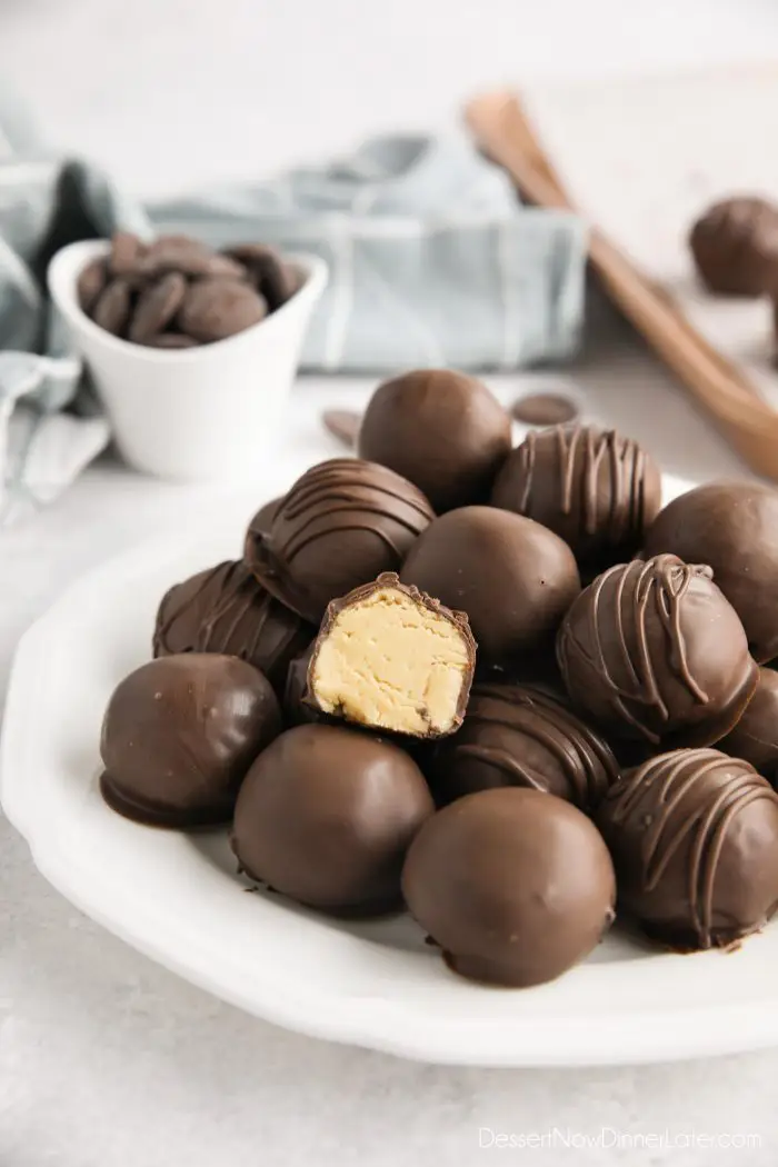 Easy peanut butter balls stacked on a plate focusing in on one that has been cut in half to show the inside.