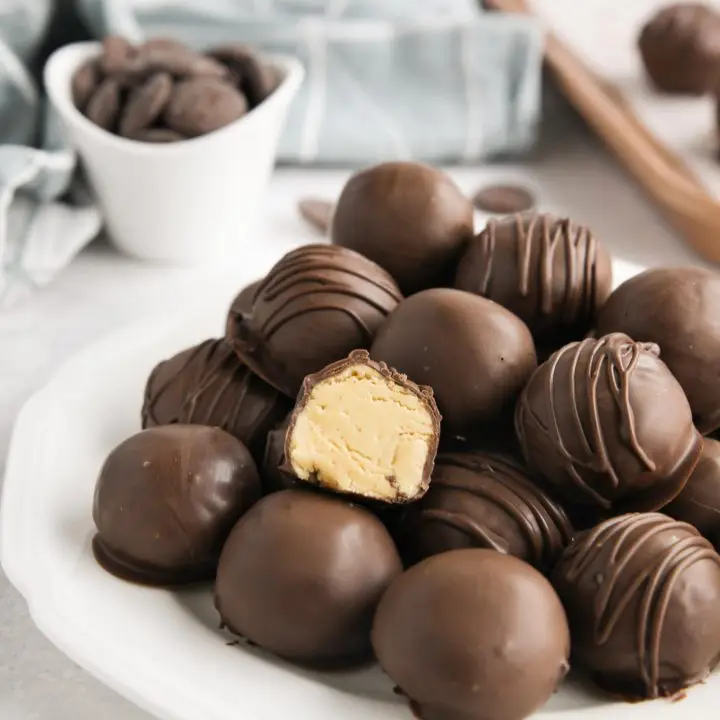 Easy peanut butter balls stacked on a plate focusing in on one that has been cut in half to show the inside.