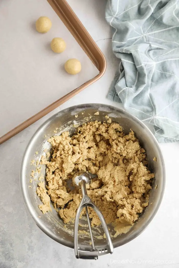 Peanut butter candy batter being scooped and rounded into balls.