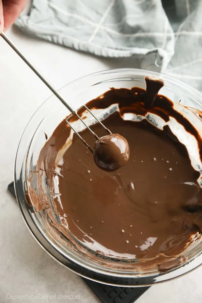 Using a chocolate dipping fork to coat a peanut butter ball in melted chocolate.