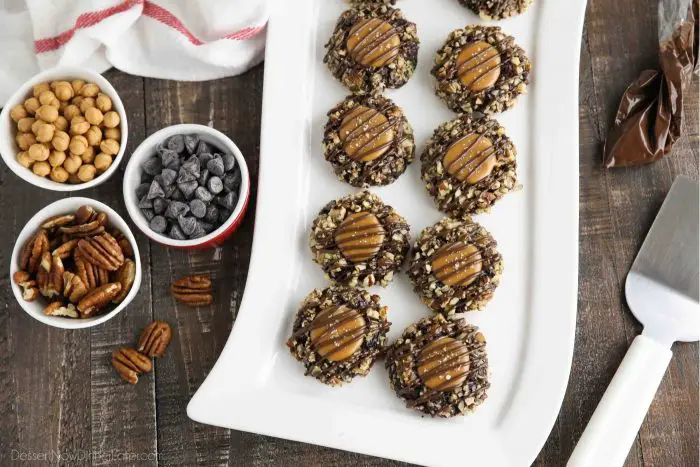 Turtle Thumbprint Cookies on rectangular plate. Pecans, caramel bits, and chocolate chips in bowls.