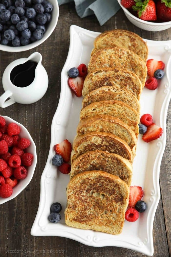 Long rectangular plate with french toast layered on top and berries on the sides.