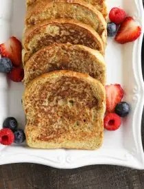 Plate of cinnamon french toast with fruit and syrup on the side.
