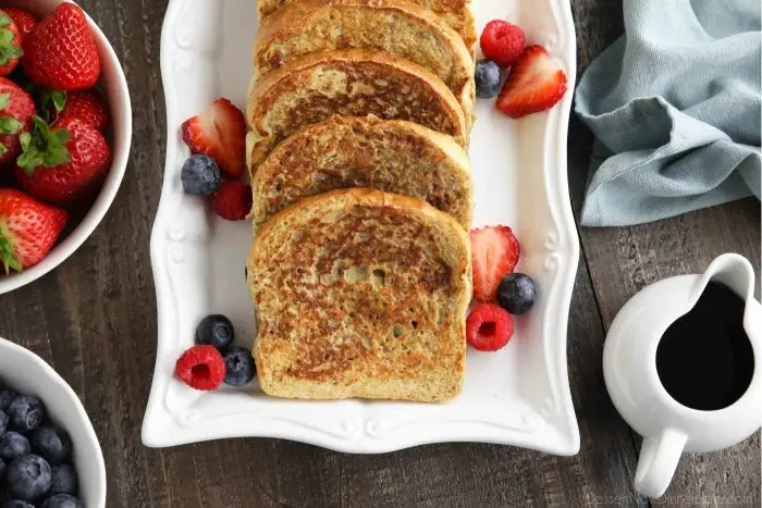 Plate of cinnamon french toast with fruit and syrup on the side.