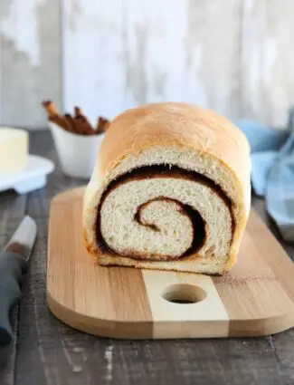 Loaf of cinnamon bread on a cutting board with a slice removed to show the cinnamon swirl on the inside..
