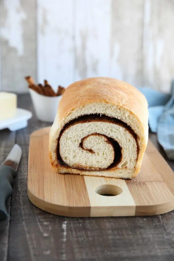 Loaf of cinnamon bread on a cutting board with a slice removed to show the cinnamon swirl on the inside..