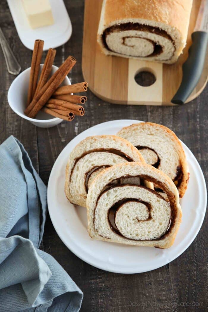 Slices of cinnamon swirl bread on a plate, with the loaf and knife on a cutting board in the background.