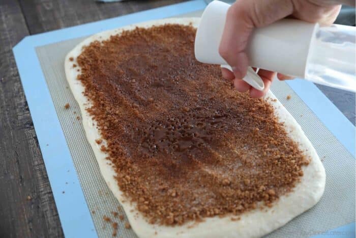 Cinnamon sugar mixture spread over the butter layer, being sprayed with water.