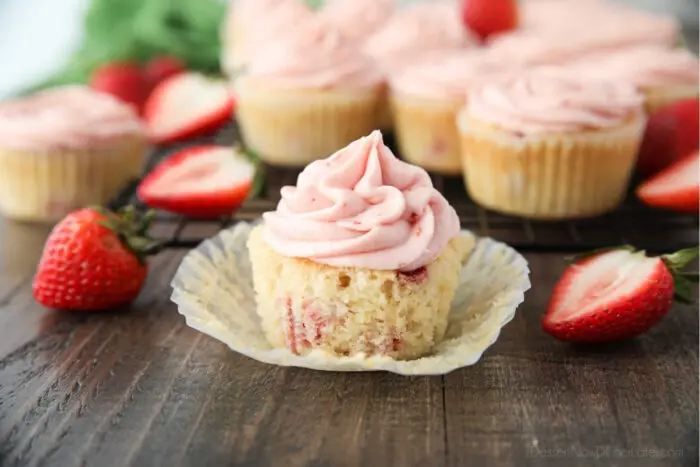 Fresh strawberry cupcake in wrapper with strawberry frosting on top.