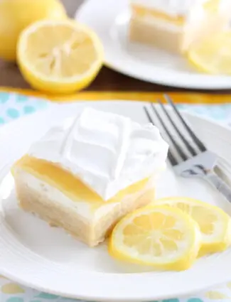 Lemon curd dessert square on plate made with a shortbread crust, sweetened cream cheese, lemon curd, and whipped cream.