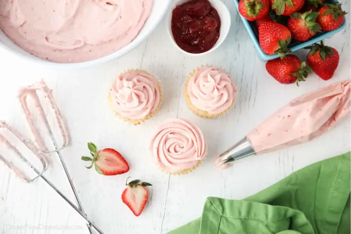 Strawberry buttercream in a piping bag with some cupcakes piped with strawberry frosting.