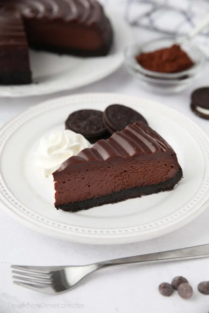 A slice of Triple Chocolate Cheesecake on a plate with Oreos and whipped cream on the side.