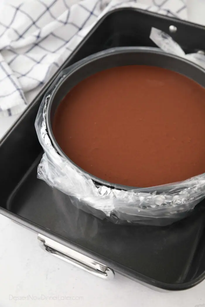 Chocolate cheesecake ready for oven, wrapped in a layer of foil, and a slow cooker plastic liner to keep water out of cheesecake.