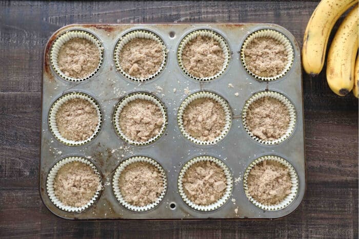 Cupcake tin filled with banana muffin batter and cinnamon streusel on top.