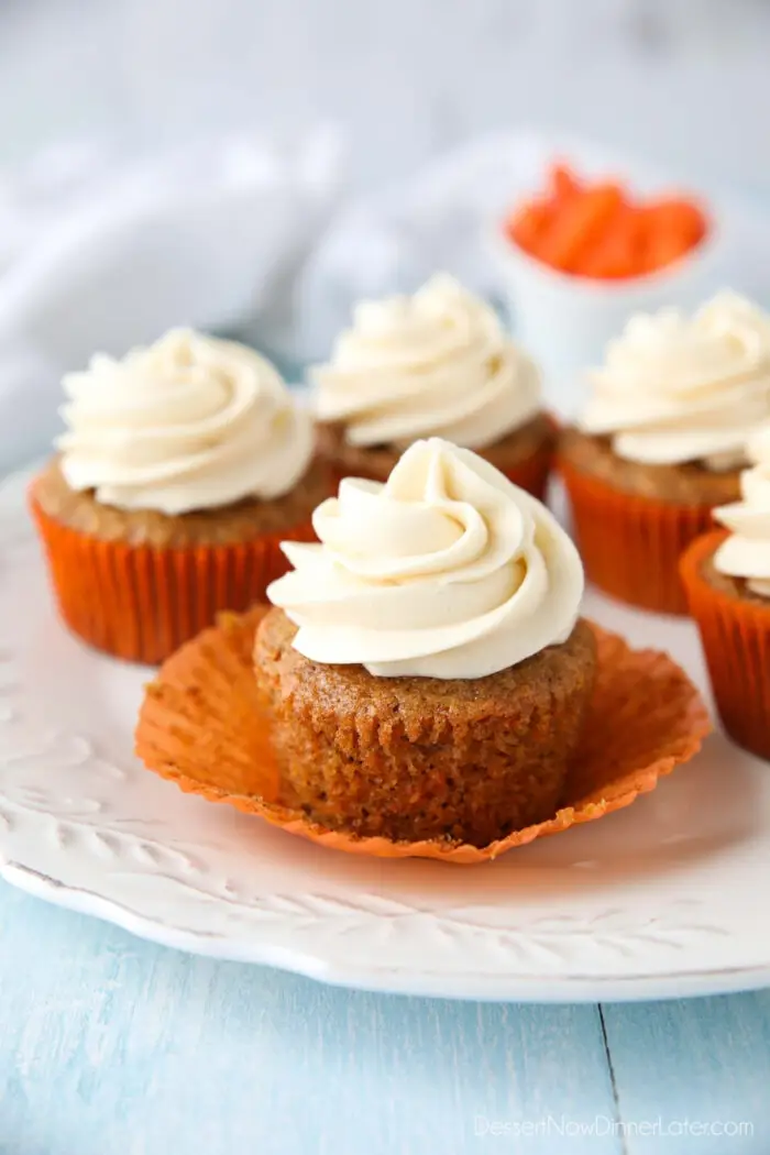 Carrot Cake Cupcakes on a plate. Focus is on a cupcake with the paper liner pulled down on the sides to show velvety texture of cake.