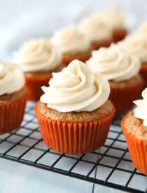 Cooling rack with cream cheese frosted carrot cake cupcakes.