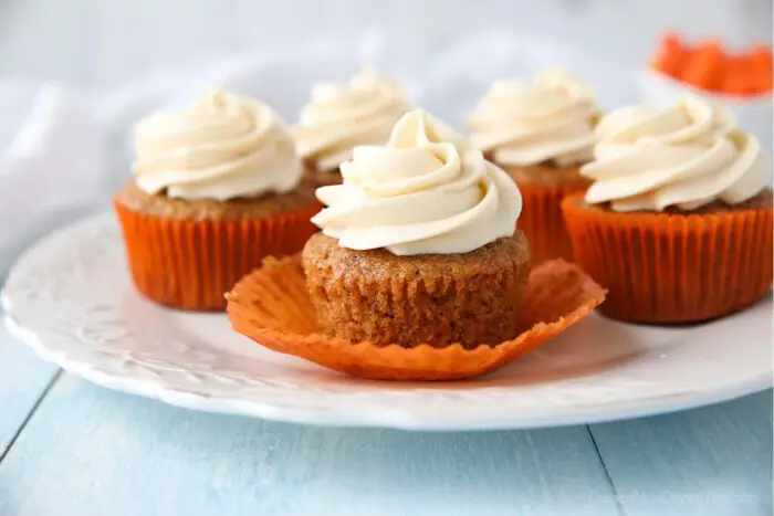 Carrot Cake Cupcakes on a plate. Focus is on a cupcake with the paper liner pulled down on the sides.