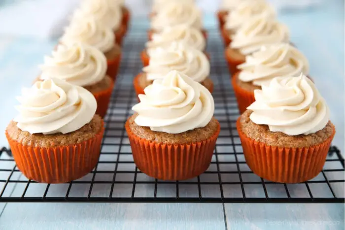 Cream cheese frosting piped on top of carrot cake cupcakes on a cooling rack.