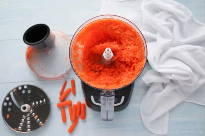 Food processor with the lid off and shredded carrots inside.